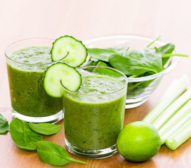 Two glass of green smoothie with spinach, celery and lime on wooden surface, with slices of cucumber on the glass