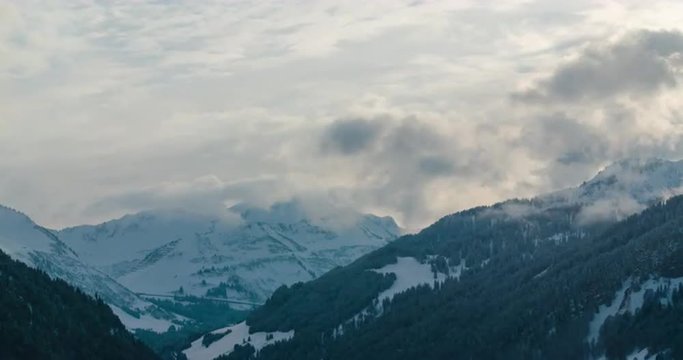 Time lapse of clouds rising from snowy forests during a sunset in Austrian Alps with snowfall in foreground