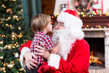 Fototapeta na wymiar Child toddler boy kissing Santa Claus sitting near Christmas tree