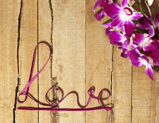 Twisted ribbon word Love with orchids on wood
