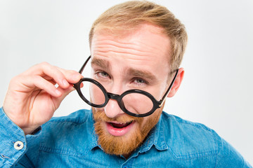 Amusing happy man with beard looking over his round glasses