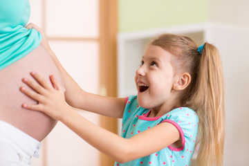 Happy child girl embraces her pregnant mother 