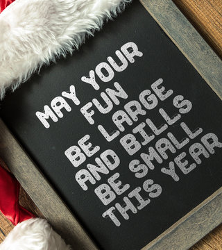 May Your Fun Be Large And Bills Be Small This Year written on blackboard with santa hat