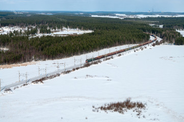 Fototapeta premium Freight train driving in snow field in northern winter forests, aerial view
