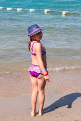 Young girl in bikini and summer hut standing on the sandy beach and looking back, full length