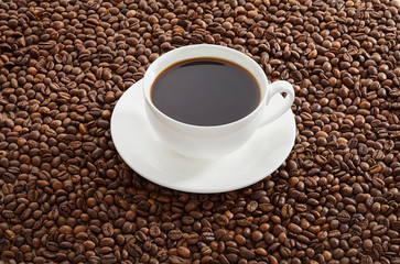 White cup of black coffee standing on roasted coffee beans.