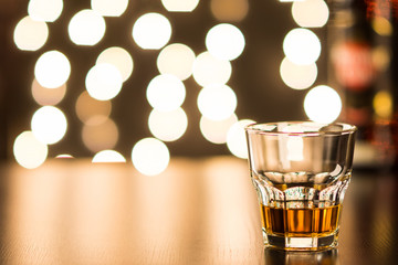 Glass with whiskey on wooden table with a beautiful bokeh in the background. Soft focus.