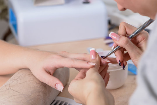 closeup of manicurist at work, painting nails in nail salon, man