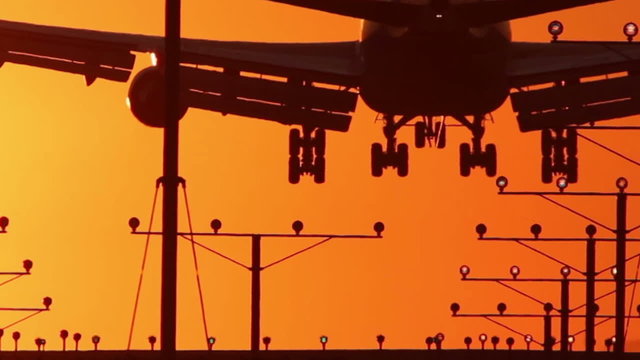 HD footage of a 4 engine jumbo jet plane framed tightly landing in silhouette against an orange sunset sky.  Jet engine audio included.