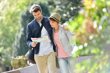 Young couple walking in park and reading city map - obrazy, fototapety, plakaty