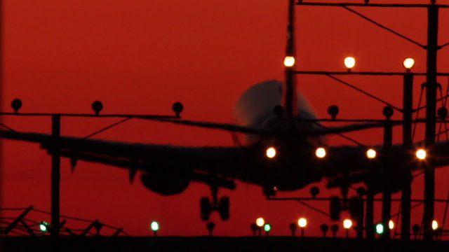 HD footage of a twin engine jet plane landing in silhouette against a red sky with visible atmospheric distortion.  Jet engine audio included