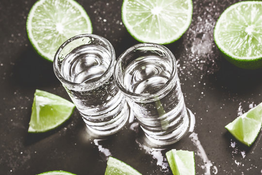 Vodka shot glass on black wet surface with limes.
