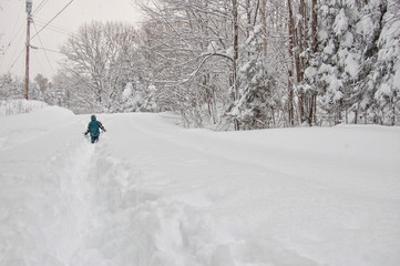 young boy walking down a snow covered rural road in a snow storm