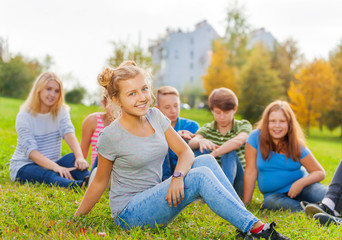 Fototapeta premium Smiling girl and friends behind sitting on grass