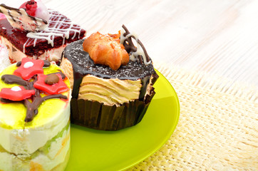 Tasty tarts, cakes with cream on green plate