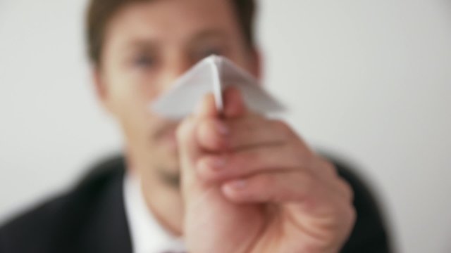 Corporate manager in modern office takes a break and prepares a paper airplane. The bored man thinks of his vacations and leans back on his chair with upset expression. Closeup shot