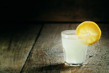 Single glass of vodka with lemon and lemon slice on an old dark