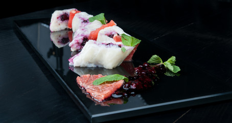 Decorated, sweet sushi rolls with blackberry served on a black plate