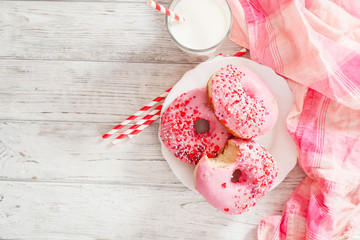 
sweet donuts with strawberry and cherry pink icing and milk on a wooden background