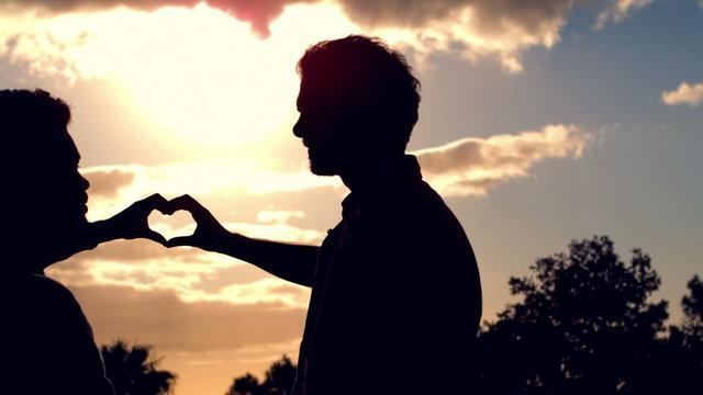 Silhouette of homosexual couple doing heart with hands together