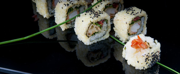 Decorated uramaki sushi served on black plate. The meal is ready for eating.