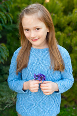 Outdoor portrait of a cute little girl of 7 years old, wearing blue pullover, holding first spring flowers violets