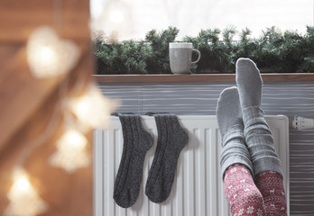 Woman warming up with feet on heater Winter woolen socks drying on a heater, christmas lights, decorations and hot drink 