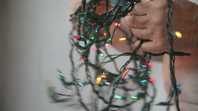 Profile view of a man trying to untangle a string of multi-colored Christmas lights
