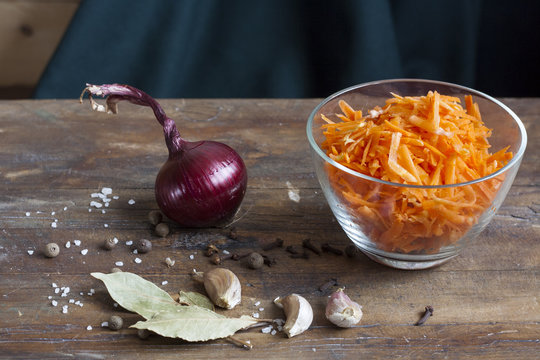 Grated carrots in bowl, spices and vegatables  on wooden table. Selective focus.