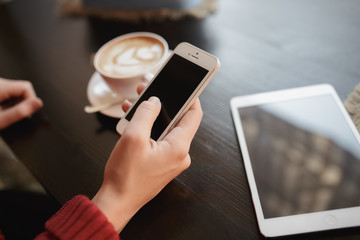 Woman's hand holding a while cellphone sitting in coffee shop