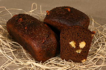 two dark bread stuffed with cheese lying in straw on grey linen