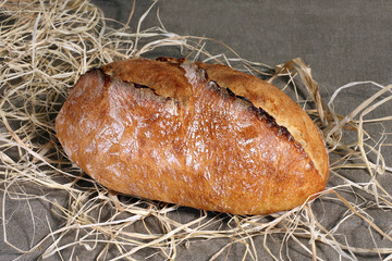 white bread lying in straw on grey linen tablecloth