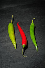 Zwei rote und eine grüne Peperoni auf einem Untergrund aus dunklem Naturschiefer