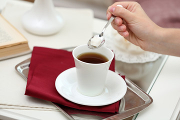 Female hand pours sugar in tea on table close up