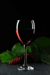 A glass of wine and red grapes, on grey-black background