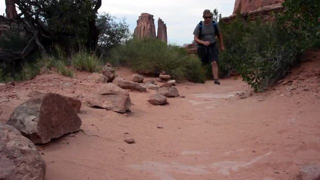 A man hikes through the Park Avenue Trail in Arches National Park toward the camera