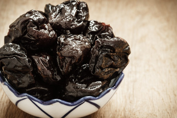 dried plums prunes in bowl on wooden table