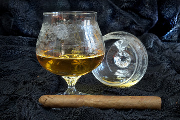 Glass of cognac with a cigar on a black velvet