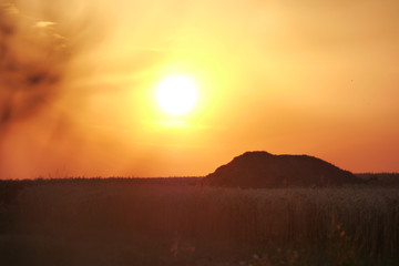A silhouette of a hill and the field surrounding it as the sun sets in the far distance
