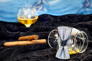 Glass of cognac with a cigar, bow tie on a black velvet with a blue backdrop