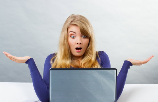 Scared woman shrugging shoulders and looking at laptop, computer problem