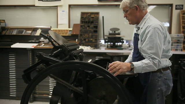 A man demonstrates the operation of a letterpress machine.
