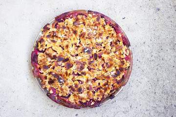 Freshly baked plum pie with almonds and crumble on top on concrete background