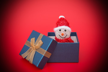 smiling toy christmas snowman in a present box on red