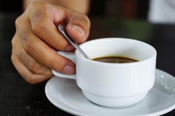 hand of man hold a spoon and coffee cup
