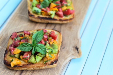 Fresh homemade rustic bruschetta with chopped red, yellow and green tomatoes, basil, olive oil and...
