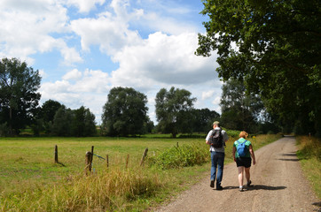 Man and woman hiking on a gravel road next to a meadow