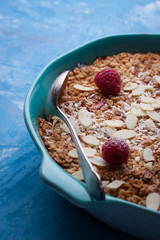 Baked oatmeal pudding with raspberries and almonds in a blue pan on a blue background. Selective focus...