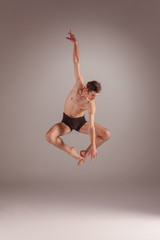 Fototapeta premium The young attractive modern ballet dancer jumping on gray background