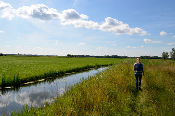 Fototapeta na wymiar Girl walking on a small trail next to a ditch in Dutch polder